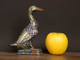 a figurine of a bird next to an apple on a table