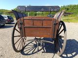a horse drawn carriage with a wooden seat on a gravel road
