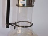 une cafetière en verre avec une poignée en métal posée sur une table