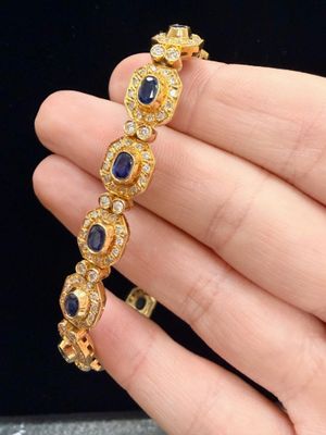 a close up of a person holding a gold bracelet with blue stones