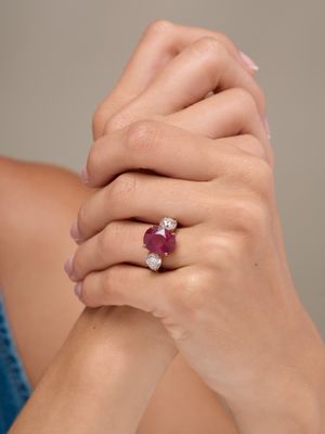 close up of a woman ' s hands holding a ring with a ruby and diamond
