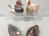 trois canards en bois posés sur une étagère transparente, posée elle-même sur une surface blanche