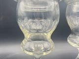 two clear glass vases with lids on a black surface