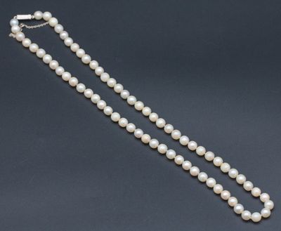 un simple rang de perles blanches muni d'un fermoir en argent sur fond noir