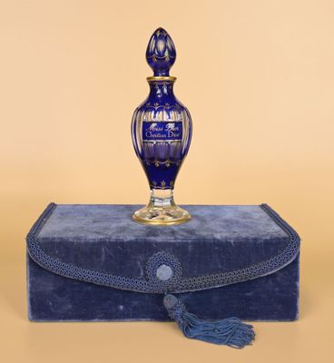 une image représentant un flacon de parfum en verre bleu posé sur une boîte bleue