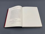 un livre ouvert posé sur une surface grise, dont la tranche est rouge