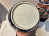 une personne tenant une tasse à la main, avec un vase en arrière-plan