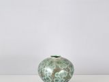 un vase vert et blanc posé sur une table blanche, sur fond blanc