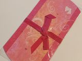 a pink card with a red bow on it on a table
