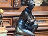 une statue représentant une femme assise sur une table, à côté d'un vase