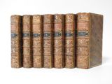 six old books are lined up in a row on a white surface