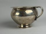 an antique silver plated sugar bowl with a handle on a white surface
