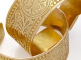 pair of gold cuff bracelets with intricate design on white background