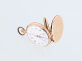 une petite montre de poche en or posée sur une surface blanche