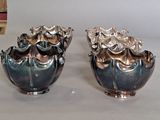 two silver vases sitting on a table with books in the background