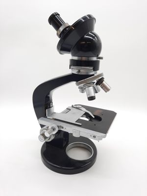 microscope noir et argenté posé sur une surface blanche, avec un fond blanc
