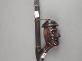 une sculpture en bois représentant un homme avec un chapeau et une canne