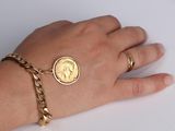 the hand of a woman wearing a gold coin bracelet and a gold chain bracelet