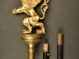 a gold statue of a lion on a pedestal next to two pencils