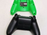 a green and black game controller next to a black controller