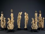 six carved ivory figurines with figures on stands on a table