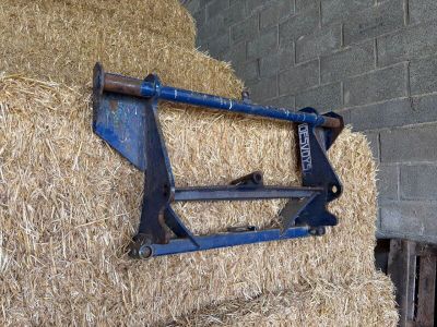 une botte de foin à laquelle est fixée une charrue bleue, dans une grange