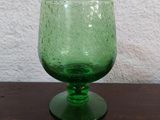 un verre vert posé sur une table, avec un mur blanc en arrière-plan