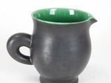 a black cup with a green handle on a white surface