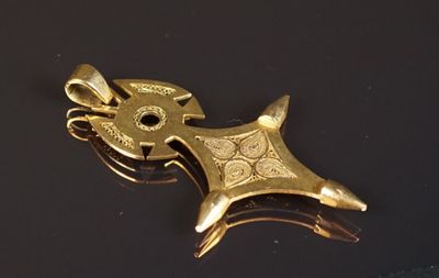 une broche en or posée sur une surface noire avec un fond noir