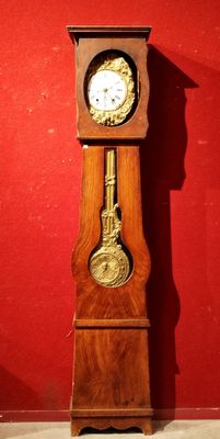 une horloge de parquet en bois exposée devant un mur rouge