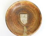 a brown plate with a crest on it on a white surface