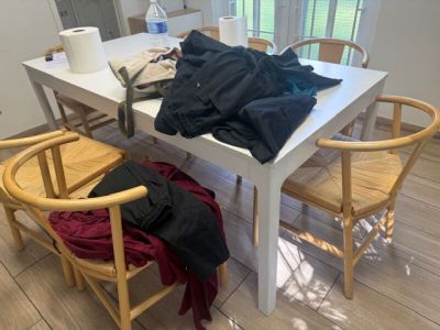 une table blanche avec deux chaises en bois et une table blanche sur laquelle est posée une chemise noire