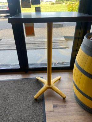 une table jaune au plateau noir, à côté d'un tonneau en bois