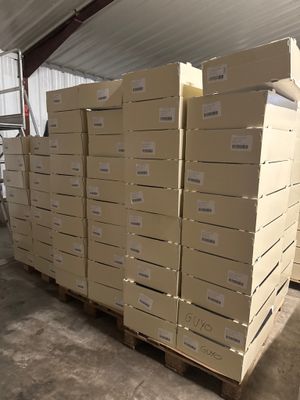 Plusieurs piles de cartons sont empilées sur des palettes dans un entrepôt