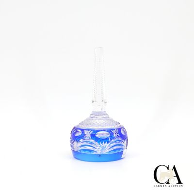 un petit vase en verre bleu muni d'une anse, posé sur une surface blanche