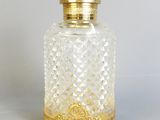 une bouteille en verre à l'ancienne avec un bouchon doré, posée sur une surface blanche