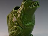 a green frog shaped vase sitting on a white surface
