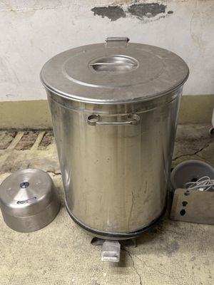 une grande casserole en métal posée par terre à côté d'une casserole plus petite