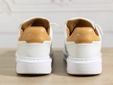 the white and tan sneakers are sitting on a wooden table