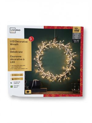 a white christmas wreath with led lights on a green background
