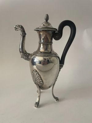 une théière en argent posée sur un socle, avec une anse noire