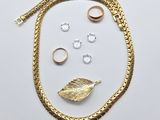 un gros plan sur un collier en or, une bague et d'autres bijoux posés sur une surface blanche