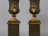 pair of antique bronze vases on pedestals on a gray background