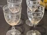 four wine glasses sitting on a table with a pitcher in the background