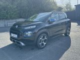 La voiture noire est garée sur le parking, à côté d'un immeuble.