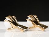 two gold hands holding an egg on a white surface