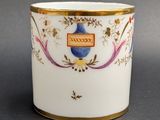 a white cup with a gold rim and a blue vase on it