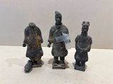 trois petites figurines représentant des hommes en costume traditionnel, posées sur une surface blanche