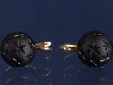 une paire de boutons de manchette noirs et dorés ornés d'un motif en forme d'étoile