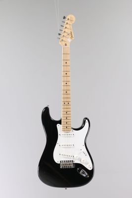 une guitare électrique noire posée sur un support, sur fond blanc